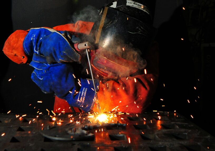 Person in Schutzkleidung mit Helm beim Elektroschweißen